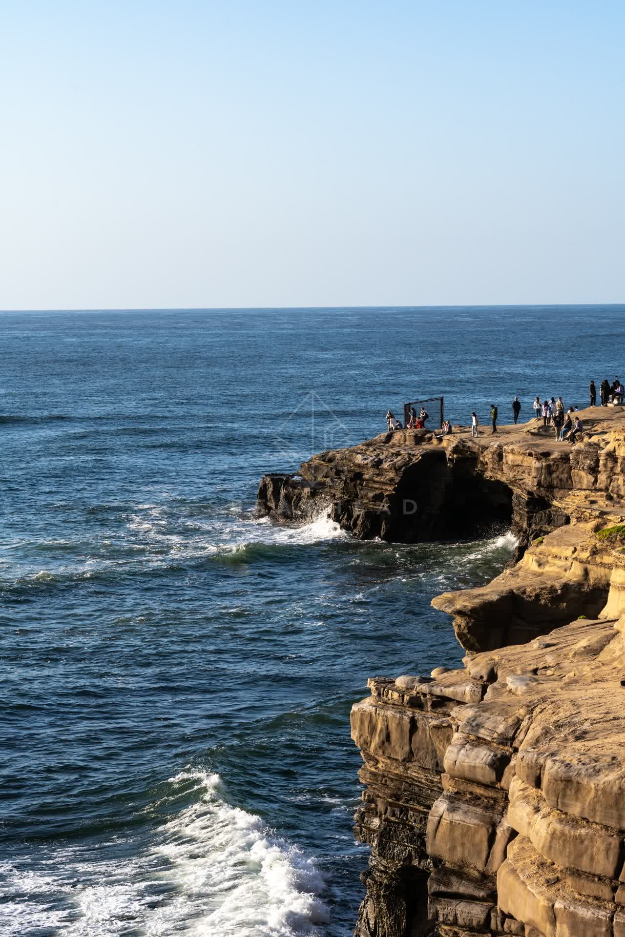 Elevated view of the cliffs, the surf and the ocean at Sunset Cliffs, with people walking.