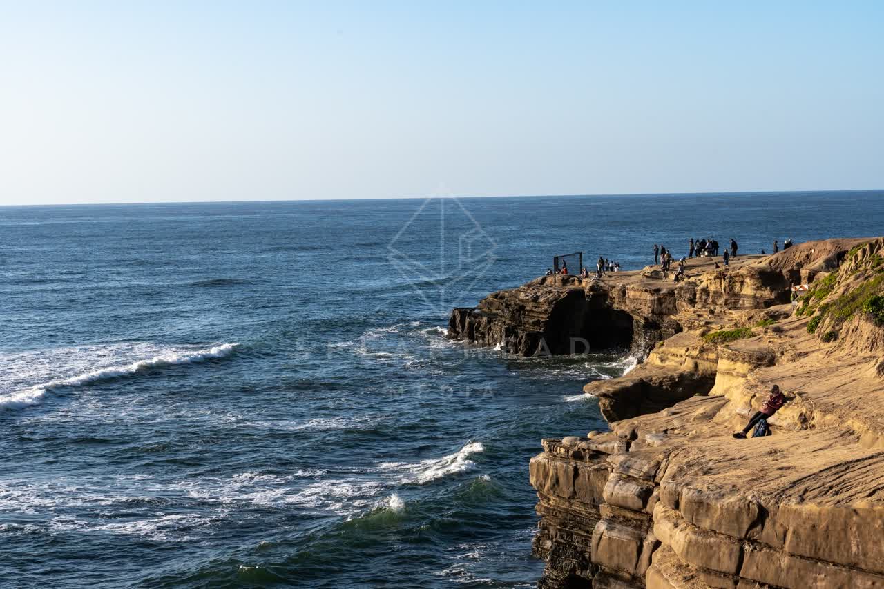 Elevated view of the cliffs, the surf and the ocean at Sunset Cliffs, with a crowd gathered.