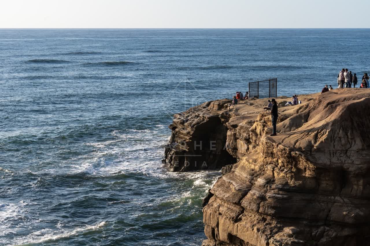 Elevated view of the cliffs, the surf and the ocean at Sunset Cliffs, with a crowd gathered.