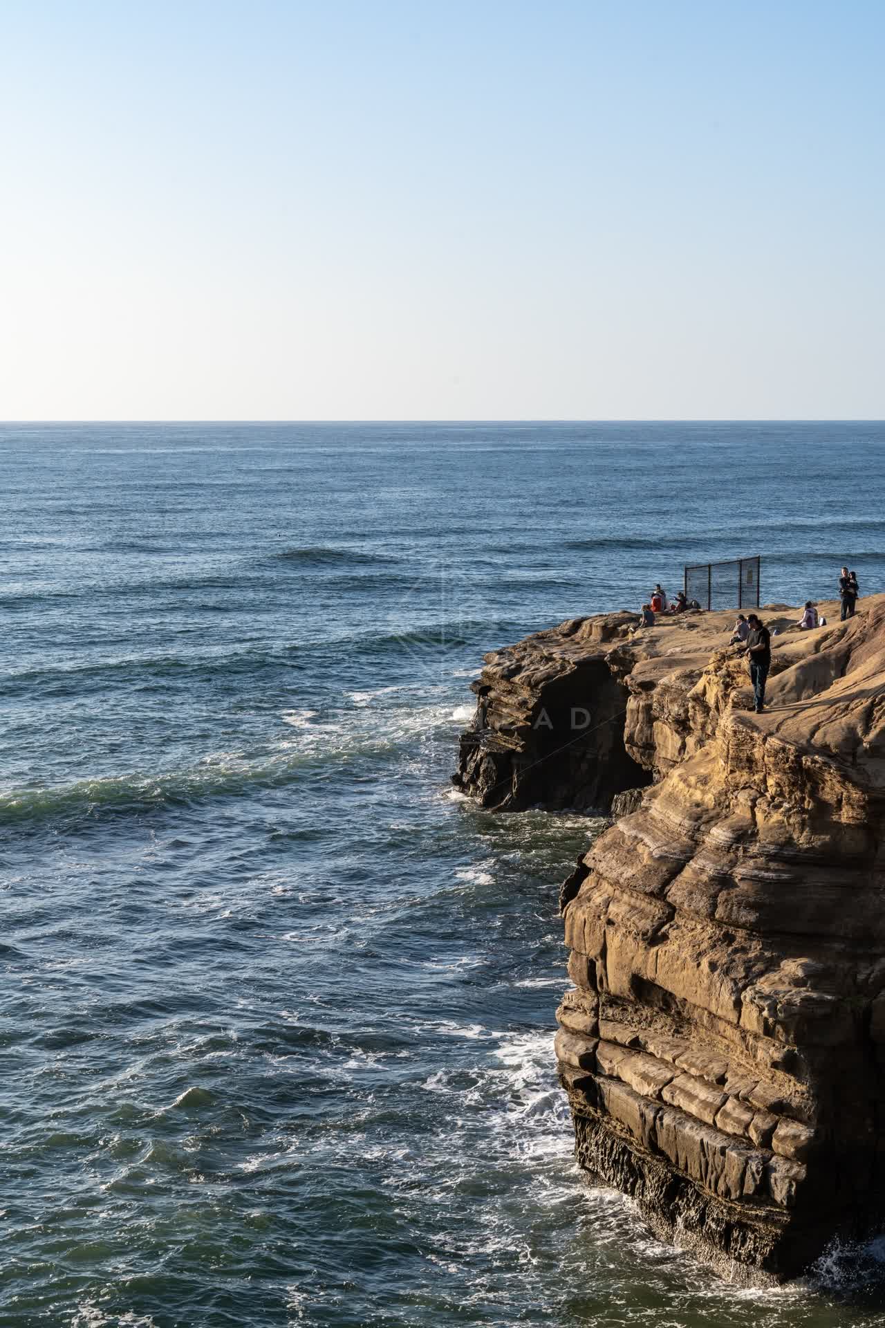 Elevated view of the cliffs, the ocean and open country at Sunset Cliffs, with people walking.