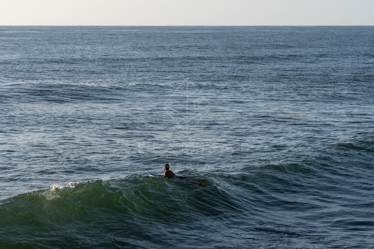 Elevated view of the beach, the surf and the ocean at Sunset Cliffs, with paddlers on the water.