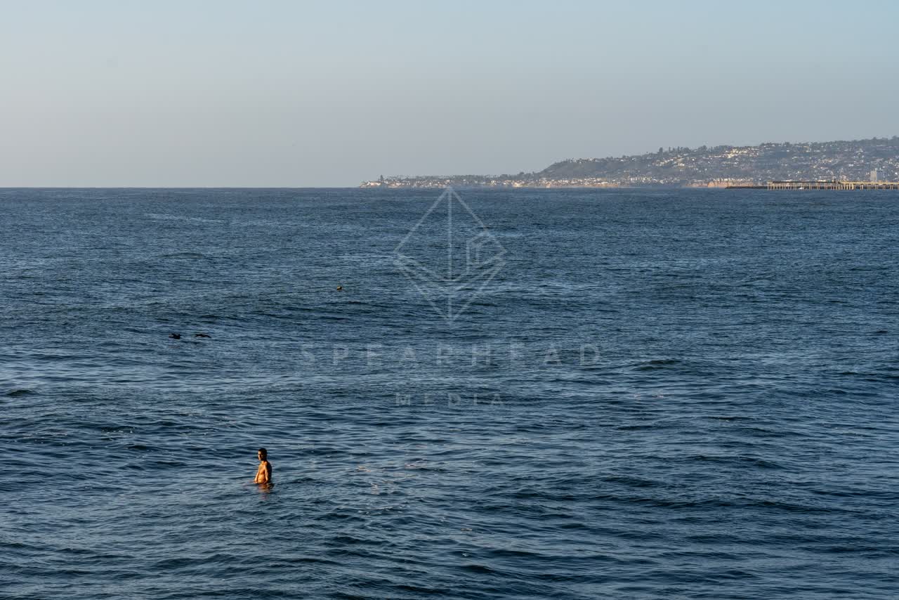 View from the water of the beach, the ocean and open country at Sunset Cliffs, with swimmers in the water.