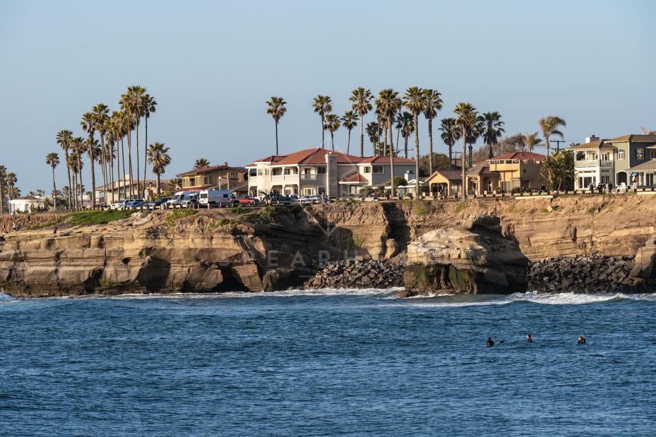 View from the water of the cliffs, palm trees and the ocean at Sunset Cliffs, with surfers out.