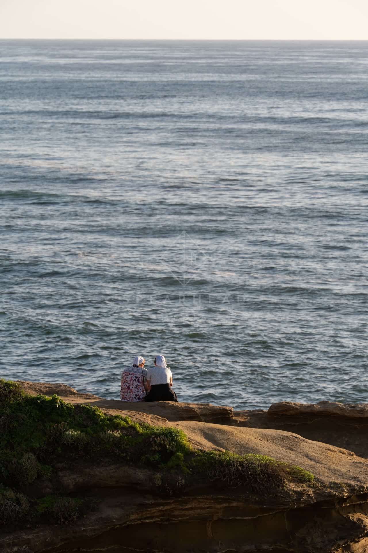 Elevated view of the cliffs, the ocean and open country at Sunset Cliffs, with people walking.