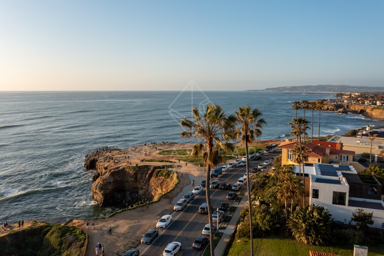 Low aerial view of the cliffs, the surf and palm trees at Sunset Cliffs, with people walking.