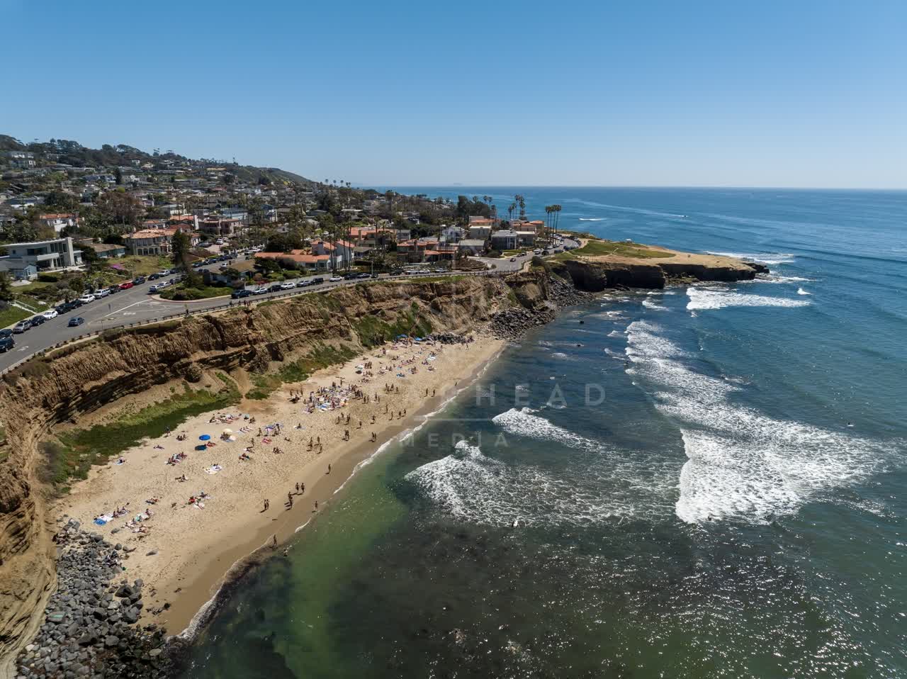 Aerial view of the beach, the surf and palm trees at Sunset Cliffs, with people walking.
