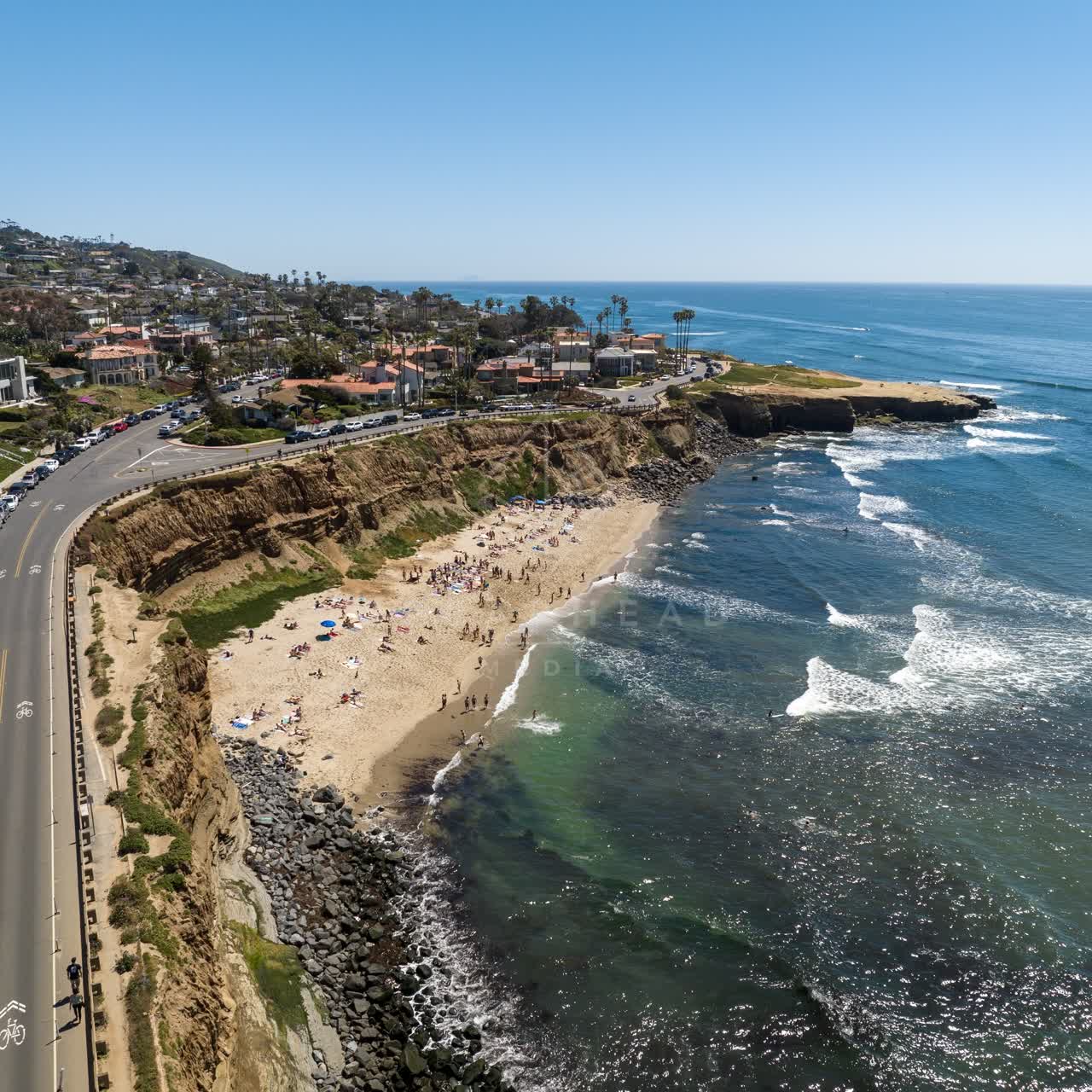 Aerial view of the cliffs, the surf and palm trees at Sunset Cliffs, with people walking.