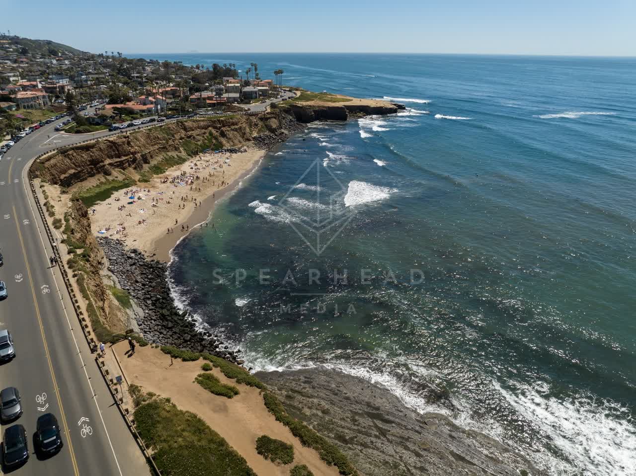 Aerial view of the cliffs, the surf and the ocean at Sunset Cliffs, with a crowd gathered.