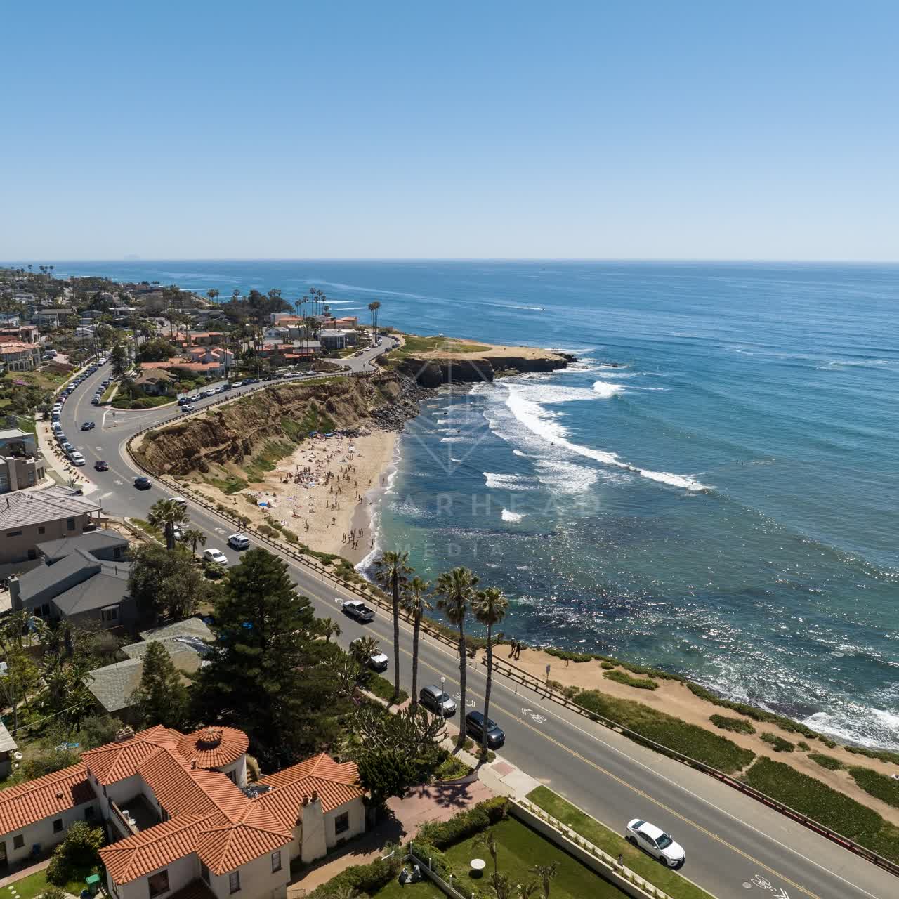 Aerial view of the cliffs, the surf and palm trees at Sunset Cliffs, with a crowd gathered.