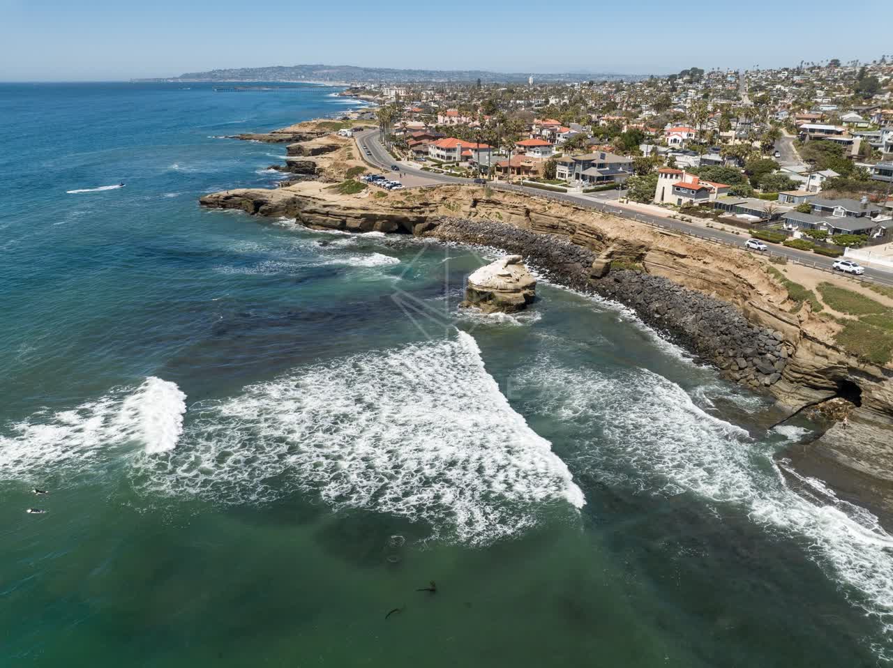 Aerial view of the cliffs, the surf and boats at Sunset Cliffs, with surfers out.