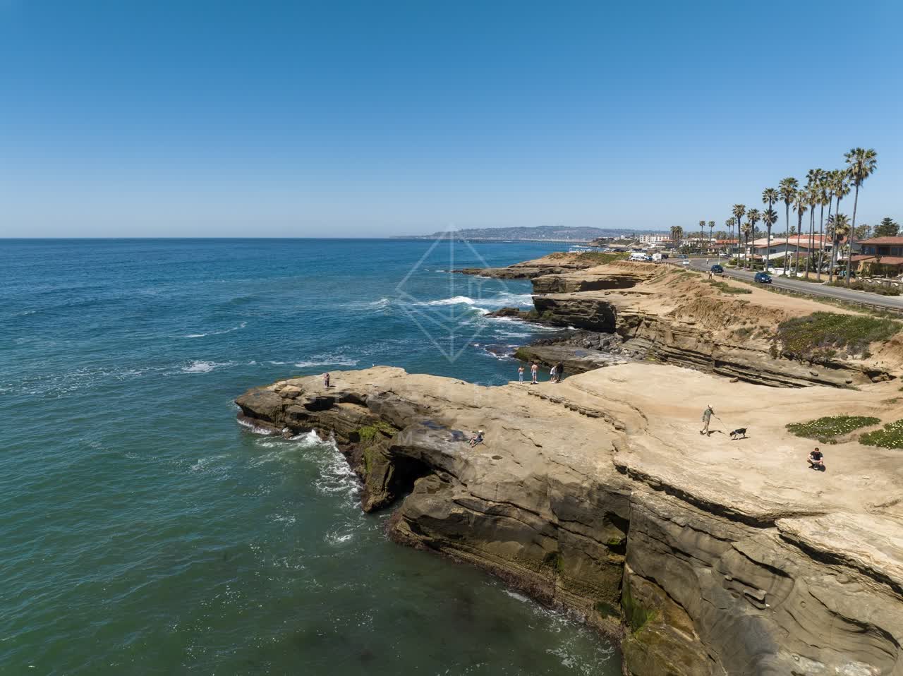 Low aerial view of the cliffs, palm trees and the ocean at Sunset Cliffs, with people walking.