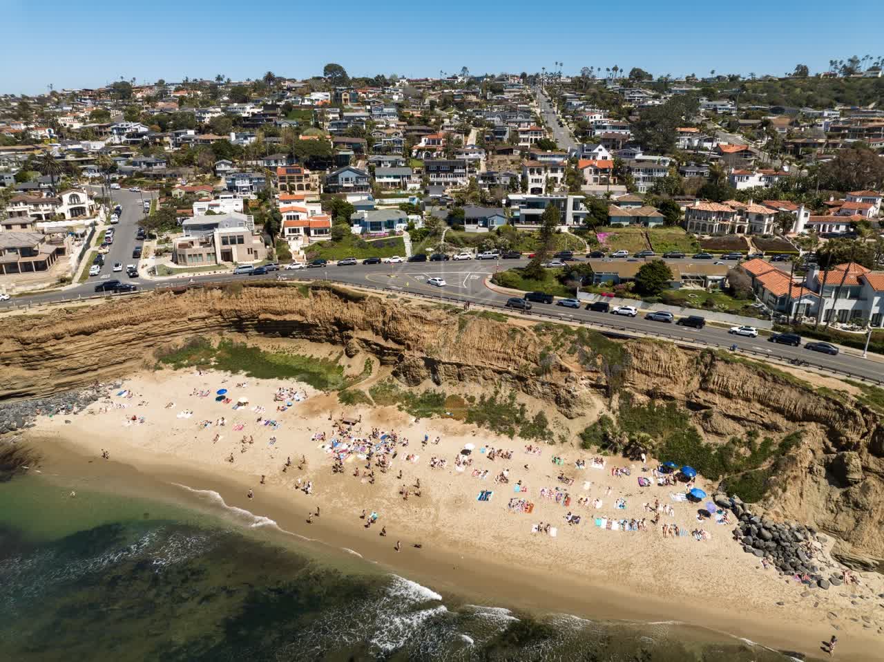 Aerial view of the cliffs, the ocean and homes at Sunset Cliffs, with a crowd gathered.