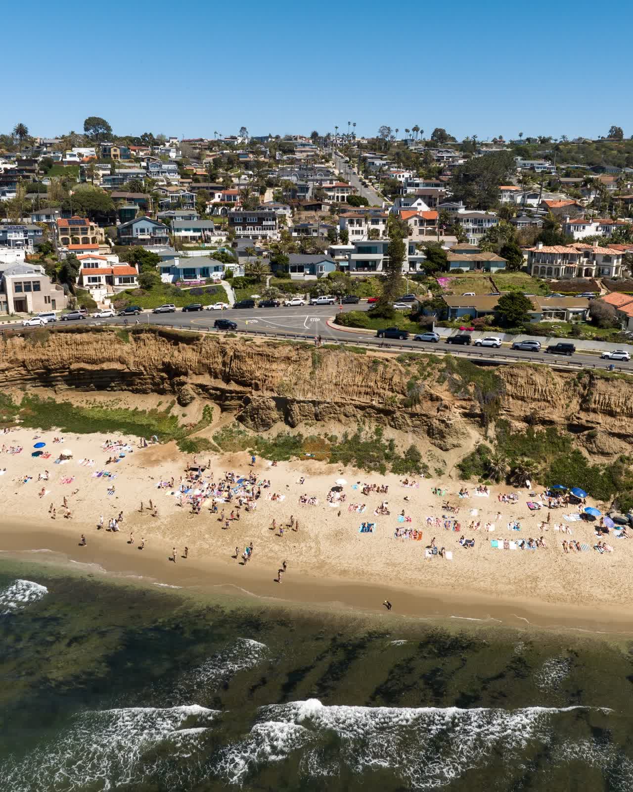 Aerial view of the beach, the surf and the ocean at Sunset Cliffs, with a crowd gathered.
