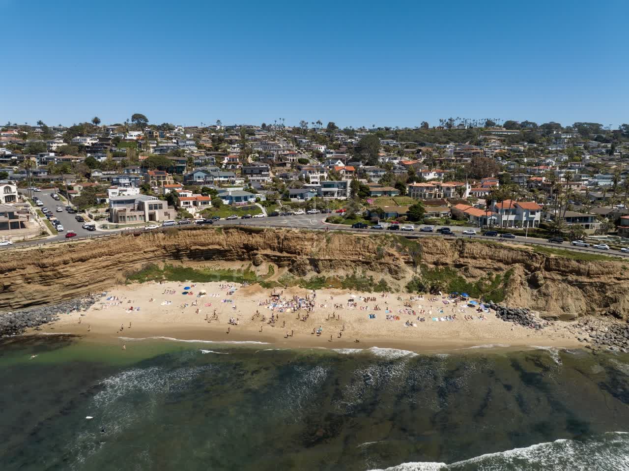 Aerial view of the cliffs, the surf and palm trees at Sunset Cliffs, with a crowd gathered.