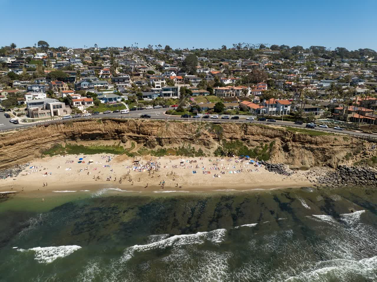 Aerial view of the beach, the surf and the ocean at Sunset Cliffs, with a crowd gathered.
