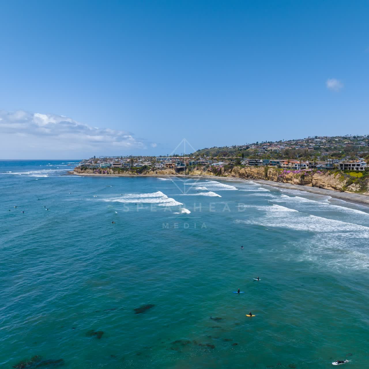 Aerial view of the cliffs, the surf and palm trees at Tourmaline, with surfers out.