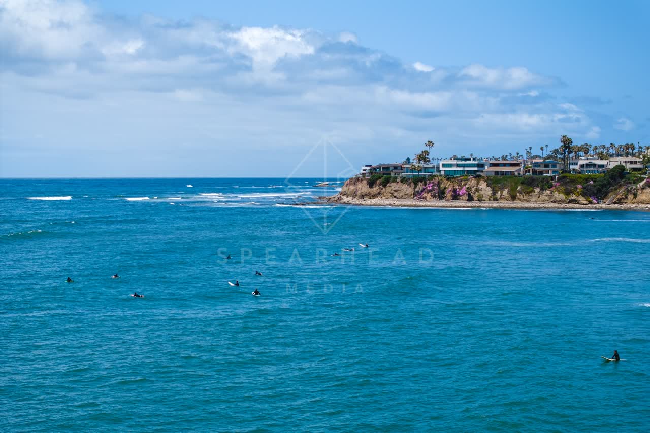 Low aerial view of the beach, the surf and palm trees at Bird Rock, with surfers out.