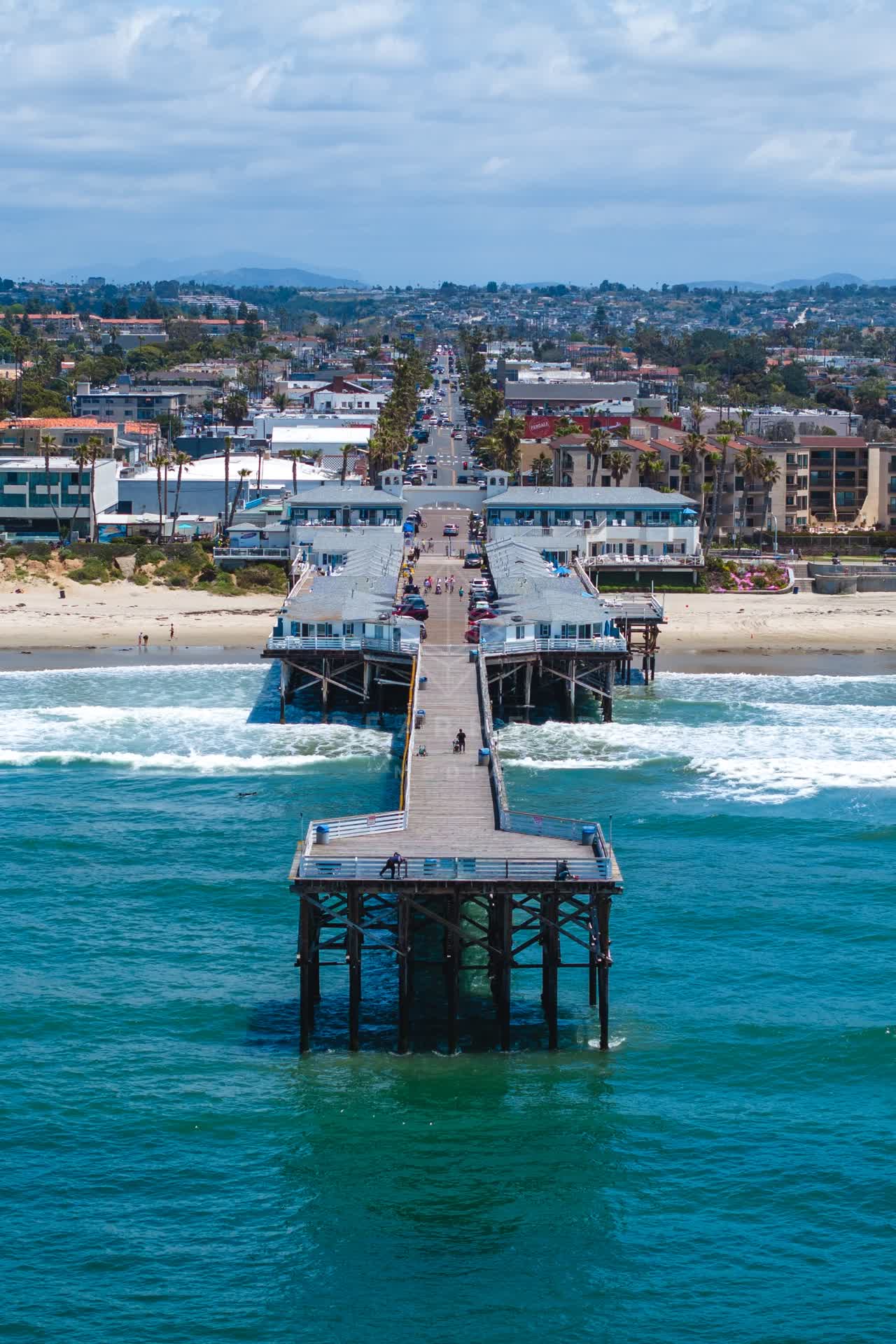 Aerial view of the beach, the surf and the pier in Pacific Beach, with people walking.