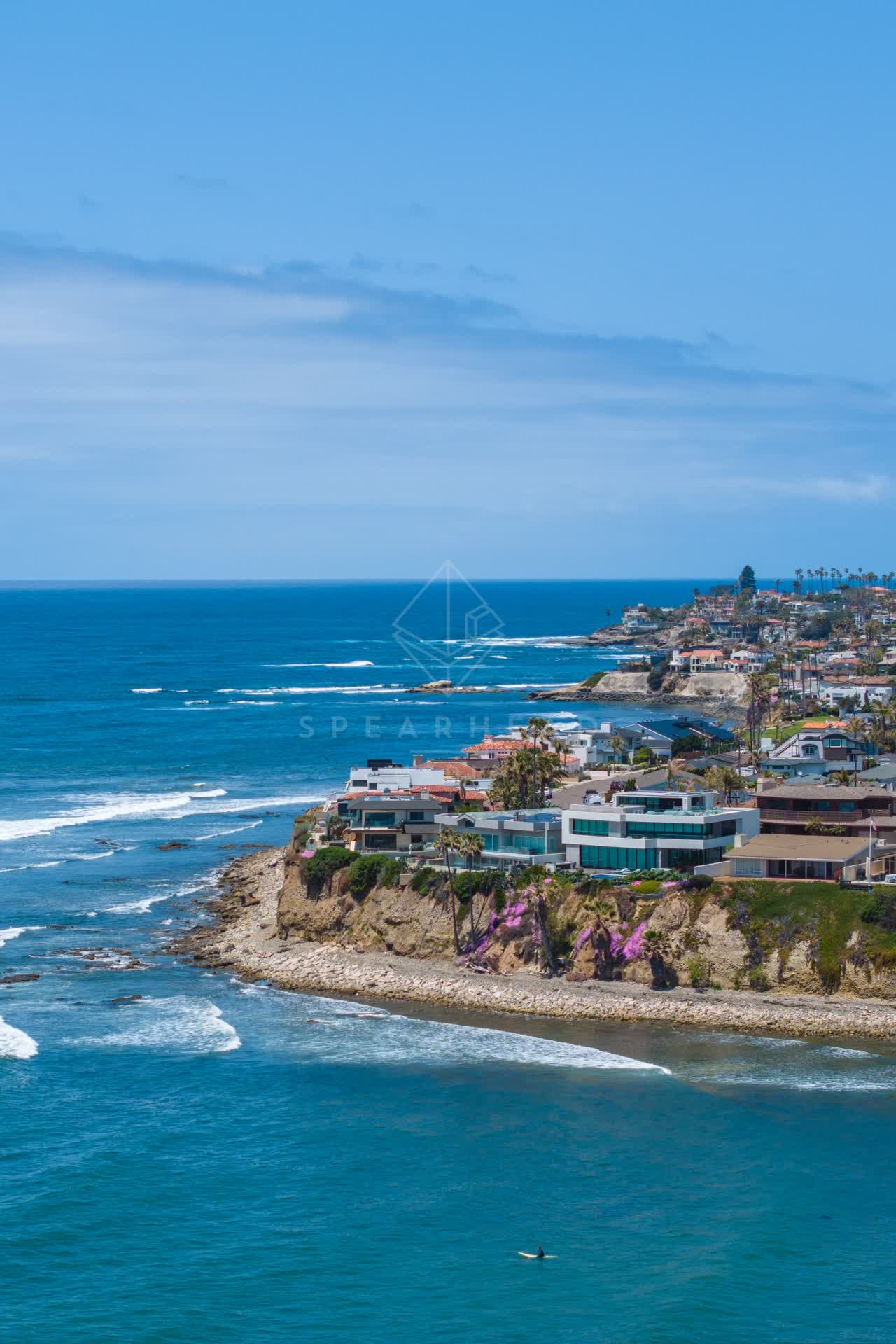 Aerial view of the cliffs, the surf and the ocean at Bird Rock, with paddlers on the water.