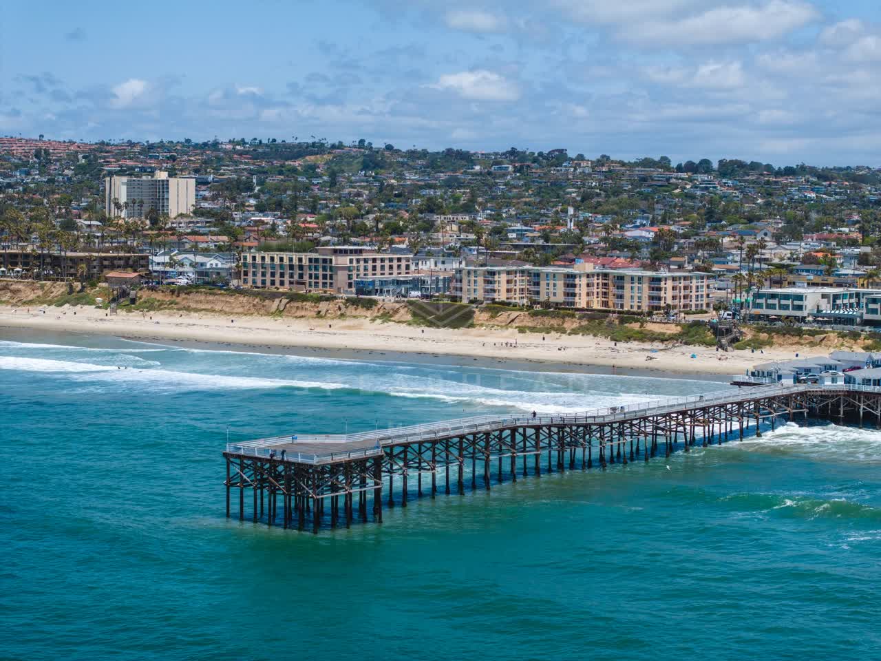 Aerial view of the beach, the surf and the pier in Pacific Beach, with people walking.