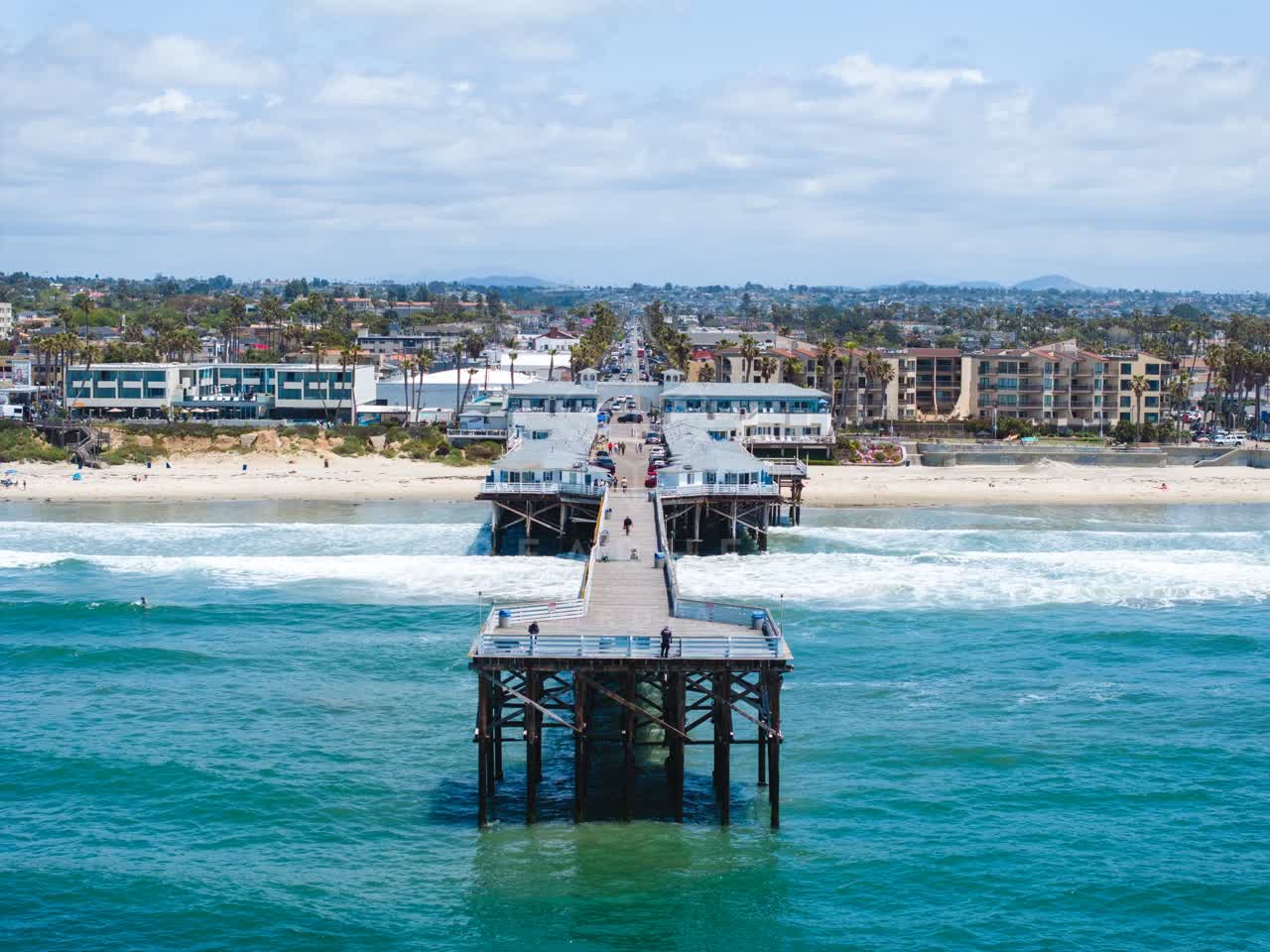 Low aerial view of the beach, the surf and the pier in Pacific Beach, with people walking.