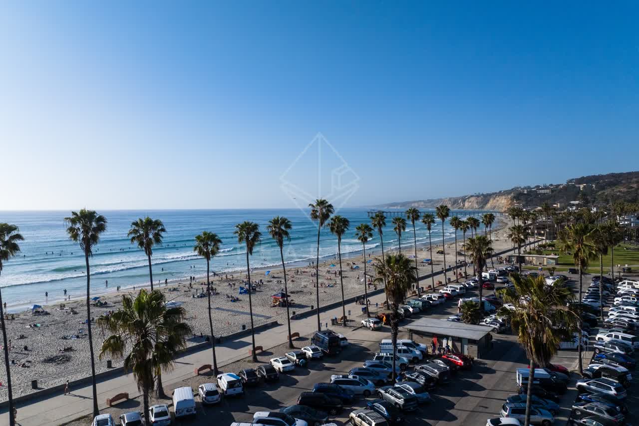 Low aerial view of the beach, the surf and palm trees at La Jolla Shores, with people walking.
