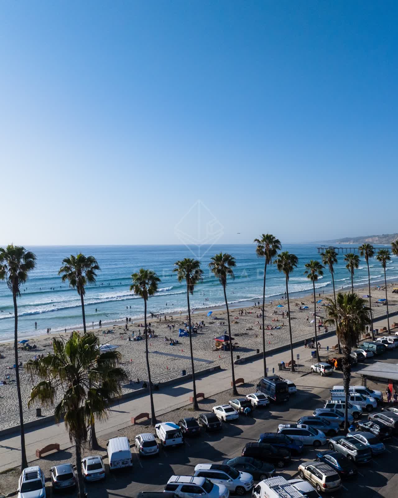 Low aerial view of the beach, the surf and the pier at La Jolla Shores, with people walking.