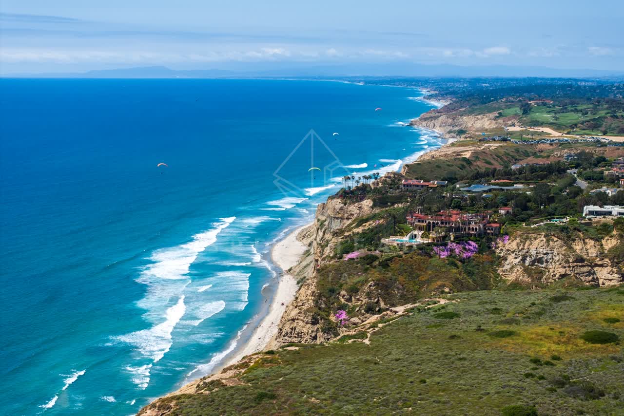 Aerial view of the cliffs, the surf and the ocean at Black’s Beach, with a crowd gathered.