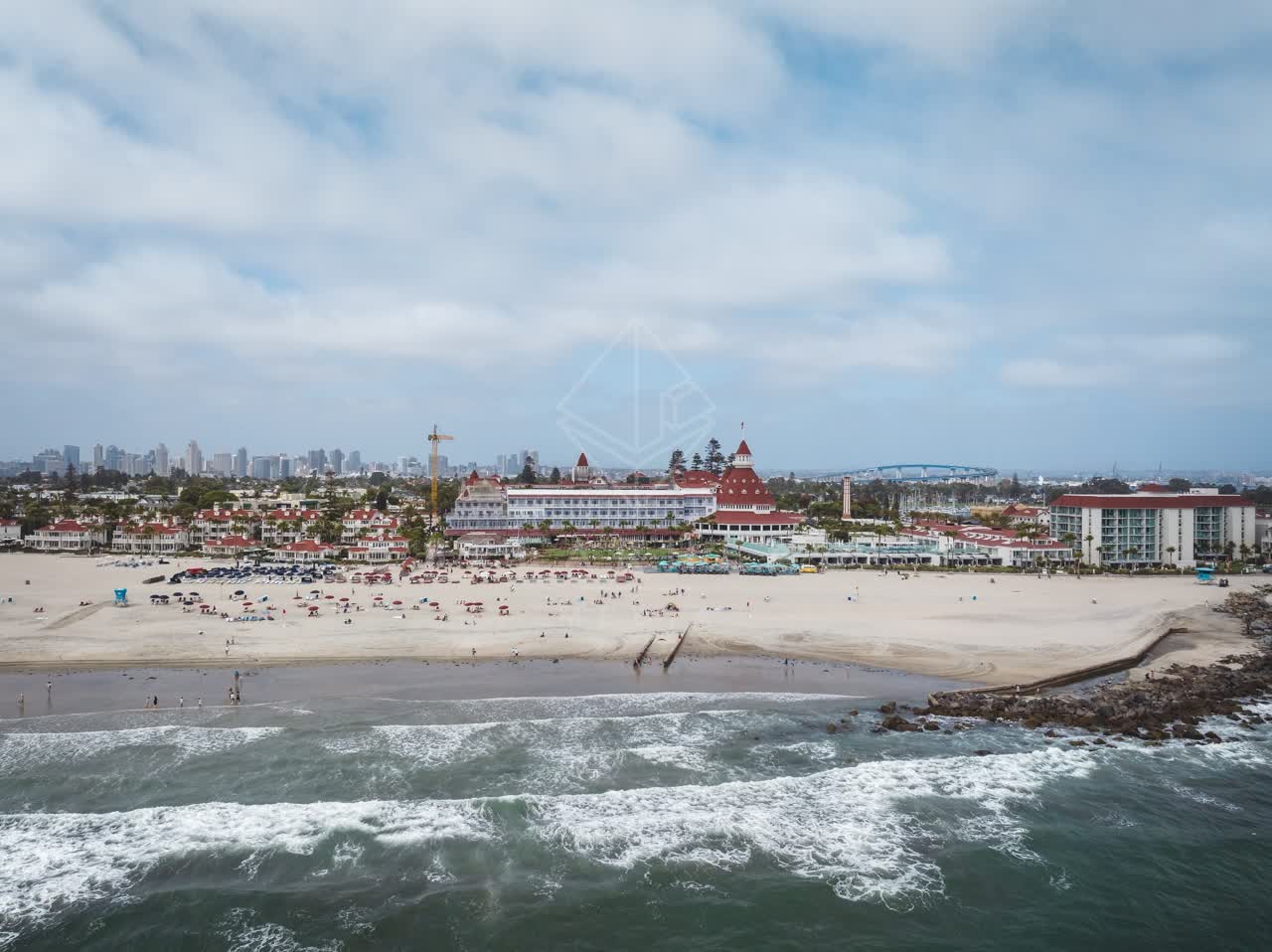 Aerial view of the beach, the surf and the bridge at Coronado Beach, with people walking.
