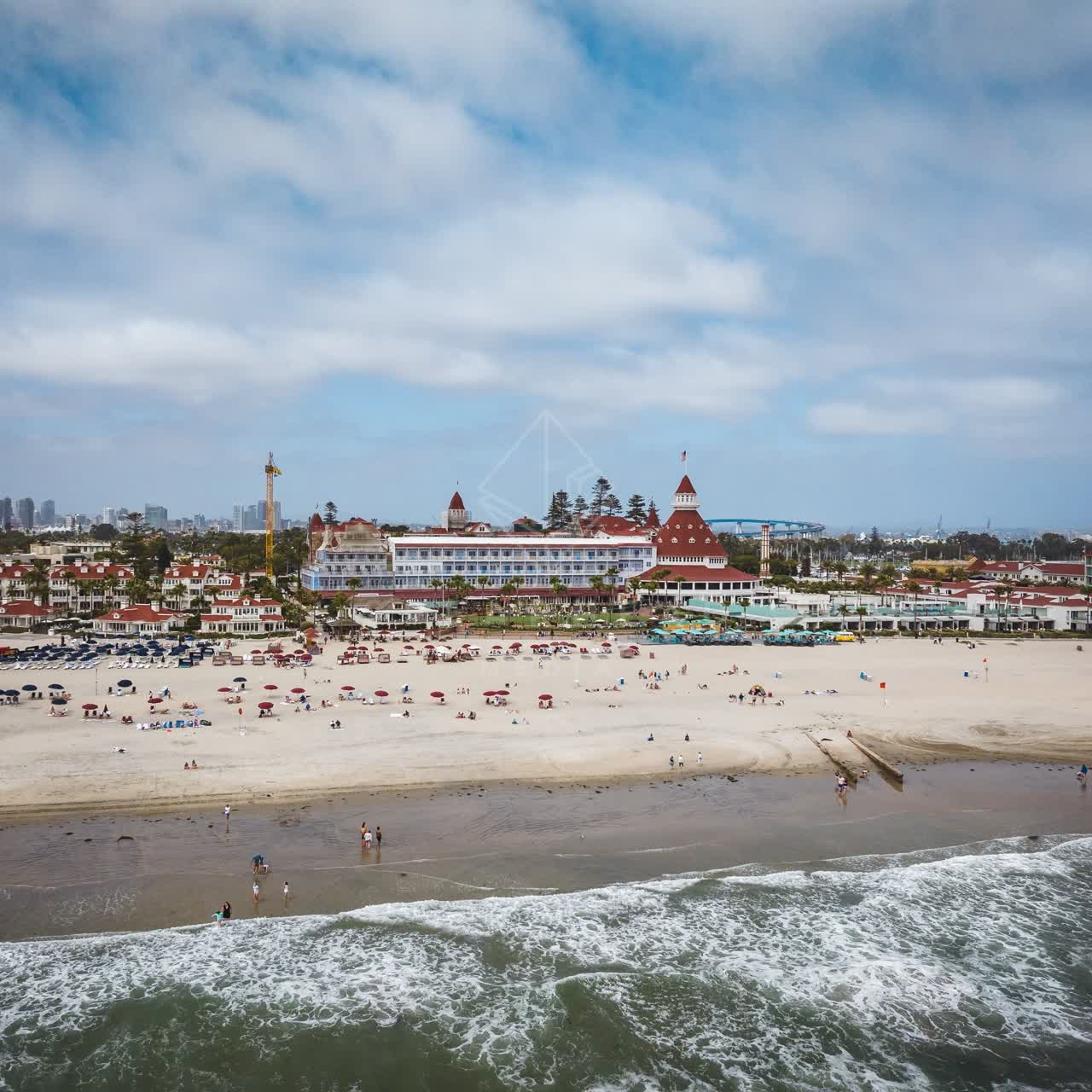 Aerial view of the beach, the surf and the bridge at Coronado Beach, with people walking.