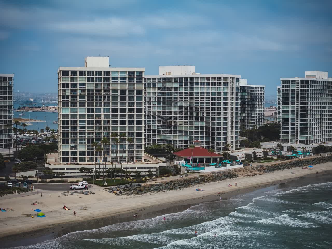 Aerial view of the beach, boats and palm trees at Coronado Beach, with people walking.