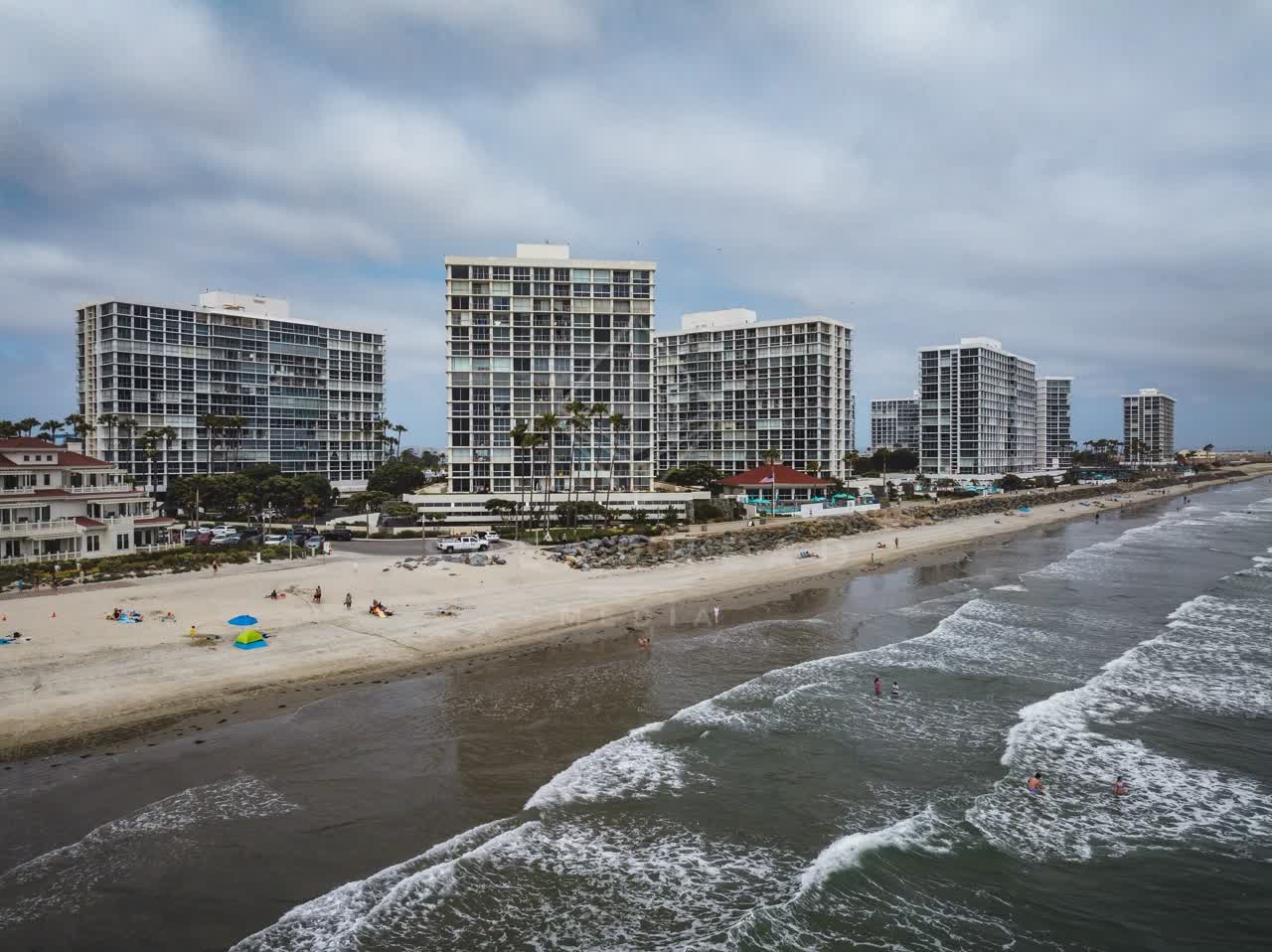 Low aerial view of the beach, the surf and palm trees at Coronado Beach, with swimmers in the water.