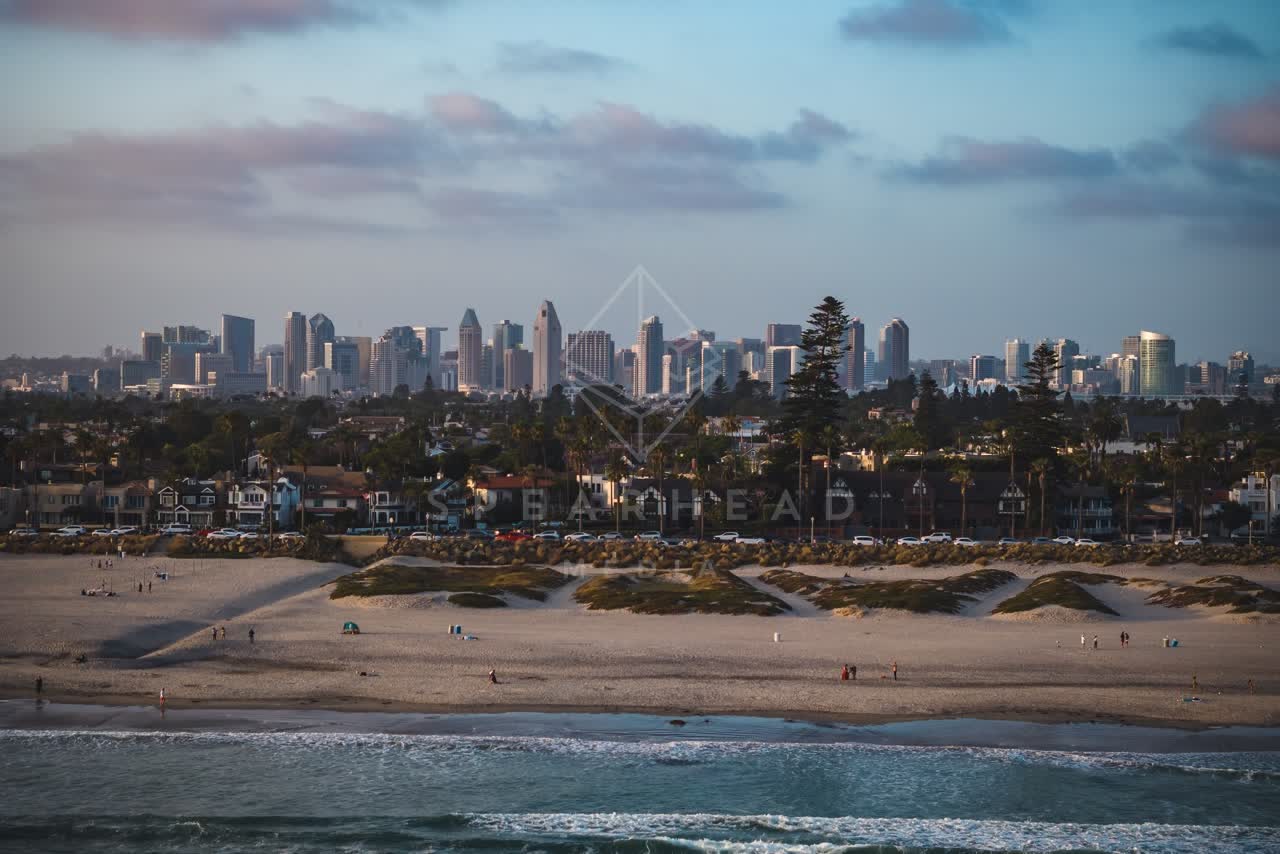 Aerial view of the beach, the surf and the skyline at Coronado Beach, with people walking.
