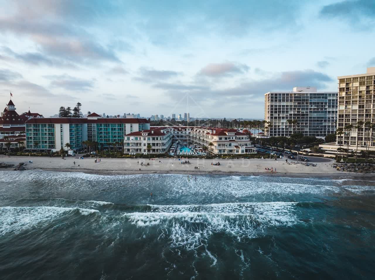 Aerial view of the beach, the surf and the skyline at Coronado Beach, with people walking.