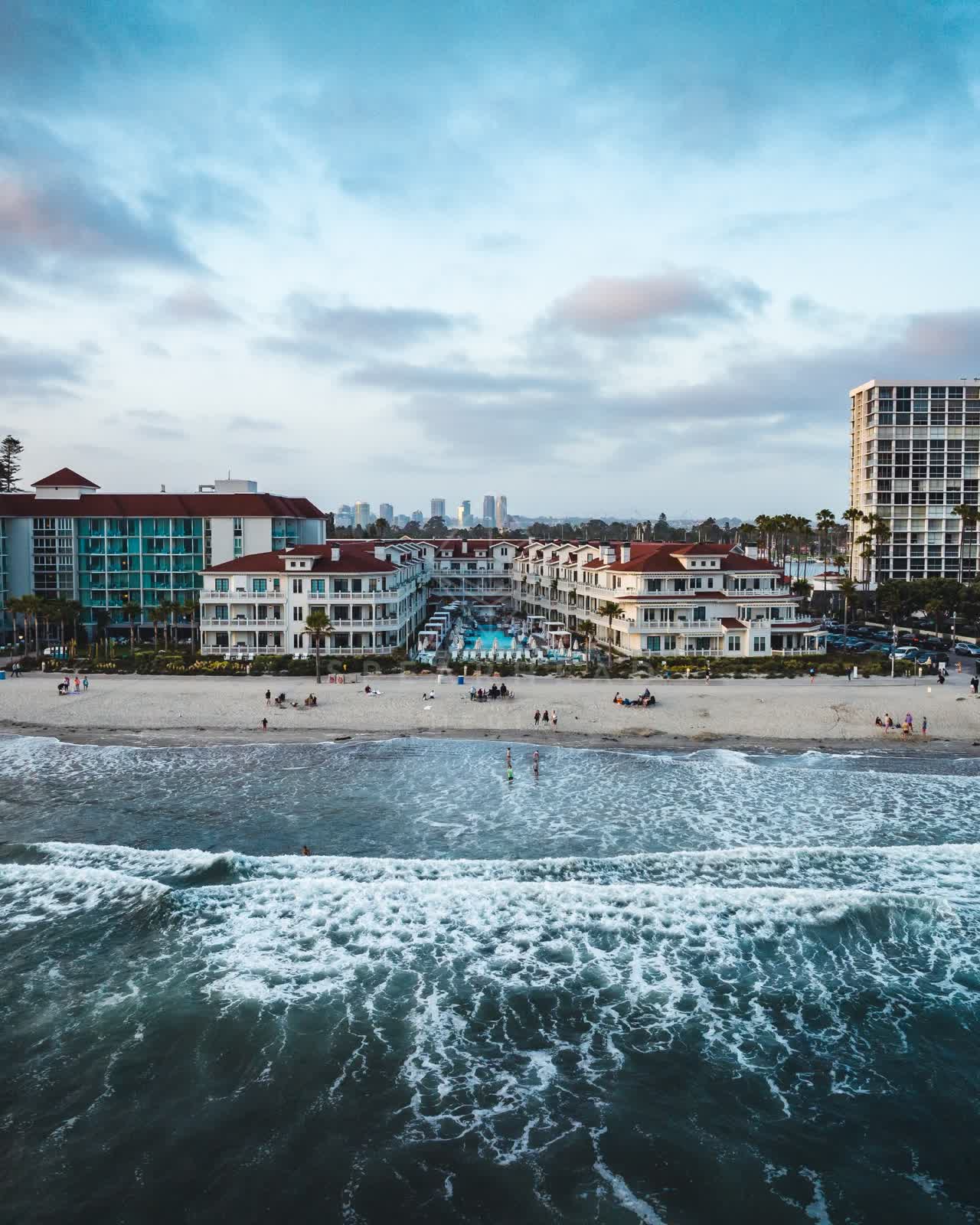 Low aerial view of the beach, the surf and the skyline at Coronado Beach, with people walking.