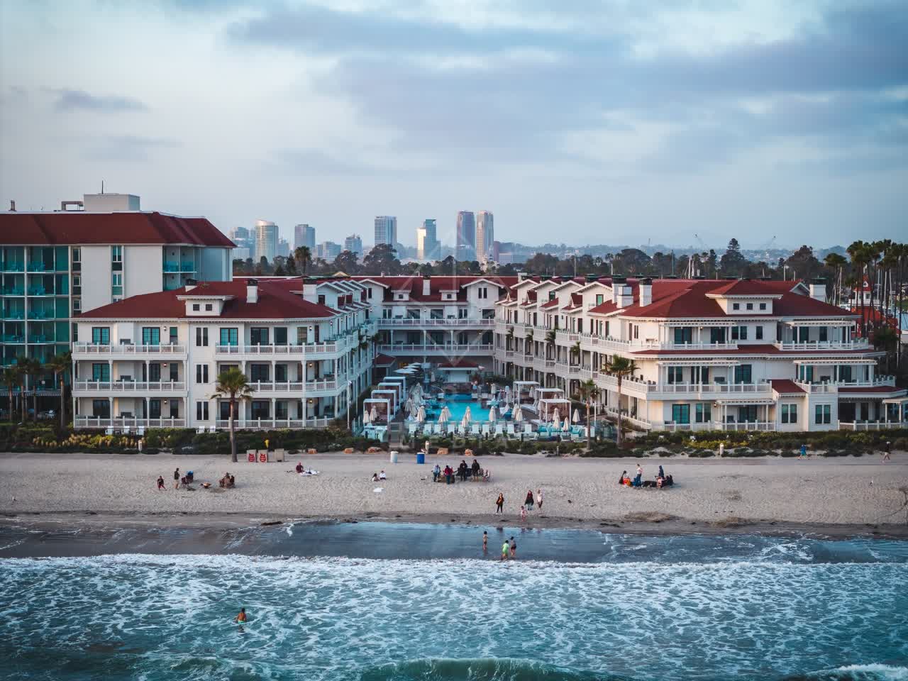 Low aerial view of the beach, the surf and the skyline at Coronado Beach, with people walking.
