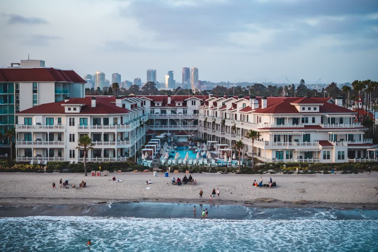 Low aerial view of the beach, the surf and the skyline at Coronado Beach, with people walking.