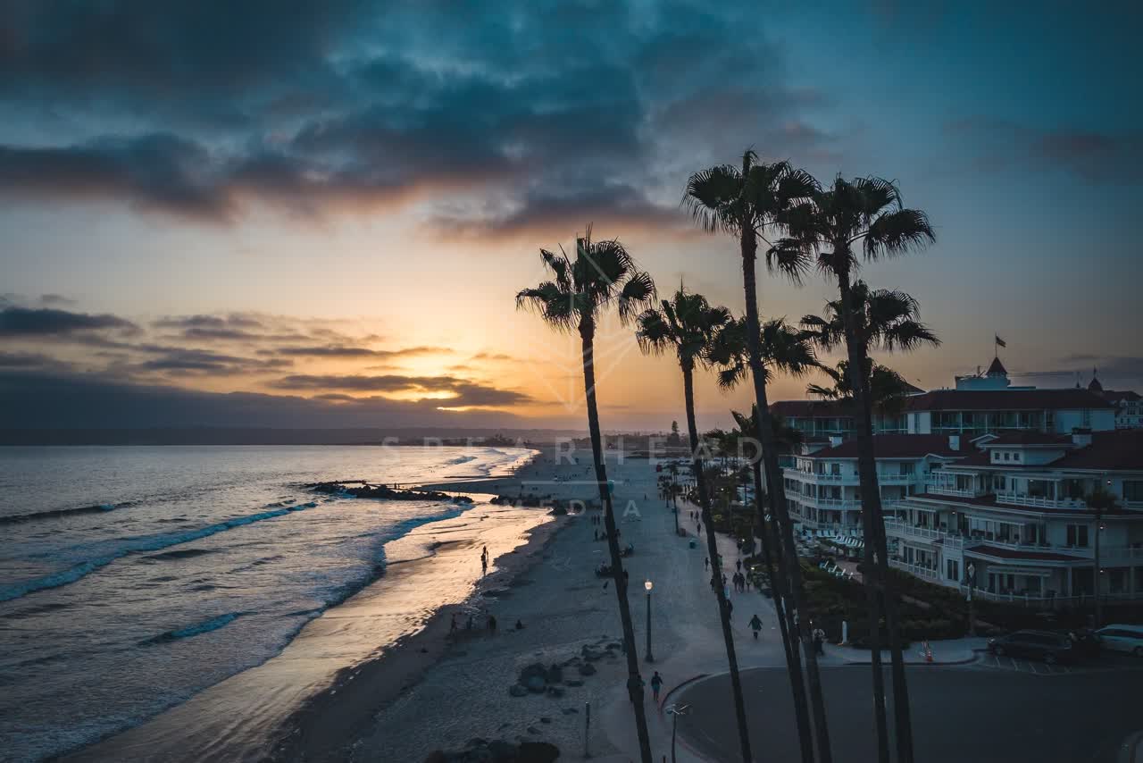 Elevated view of the beach, palm trees and the ocean at Coronado Beach, with people walking.