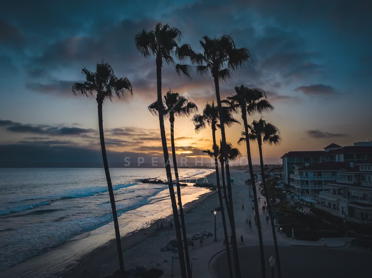 Low aerial view of the beach, the surf and palm trees at Coronado Beach, with people walking.