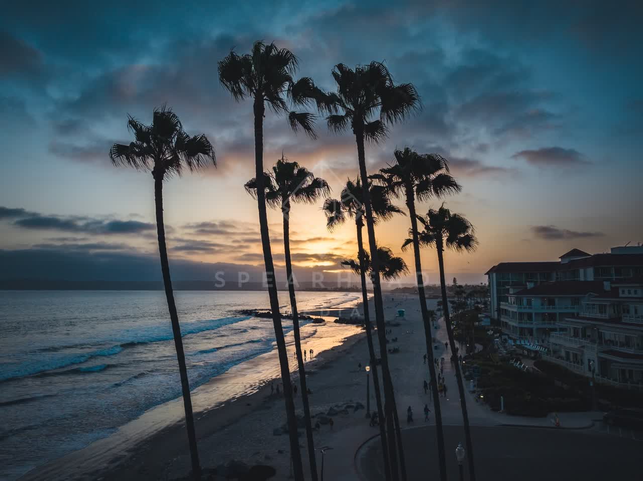 Low aerial view of the beach, the surf and palm trees at Coronado Beach, with people walking.