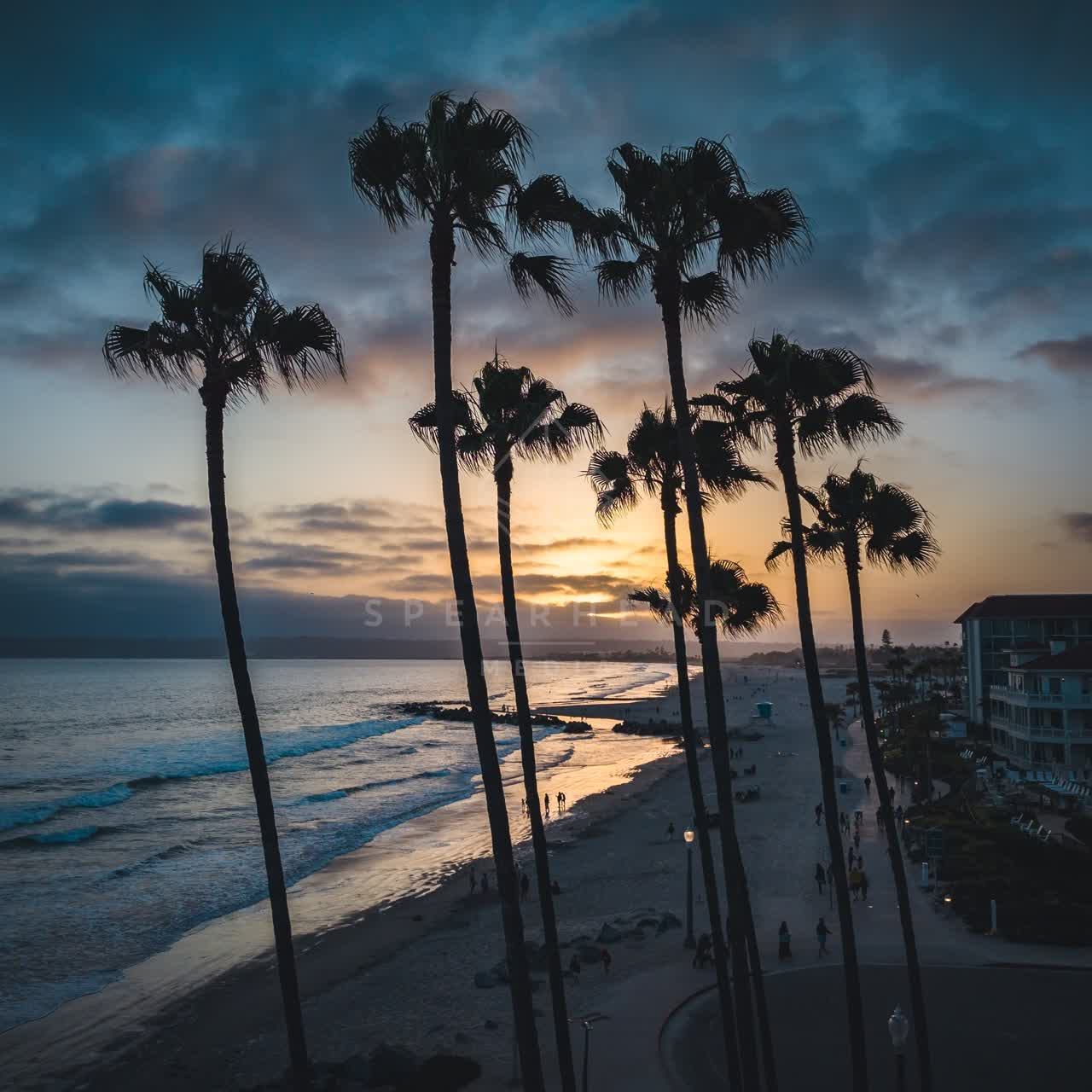 Low aerial view of the beach, the surf and palm trees at Coronado Beach, with people walking.