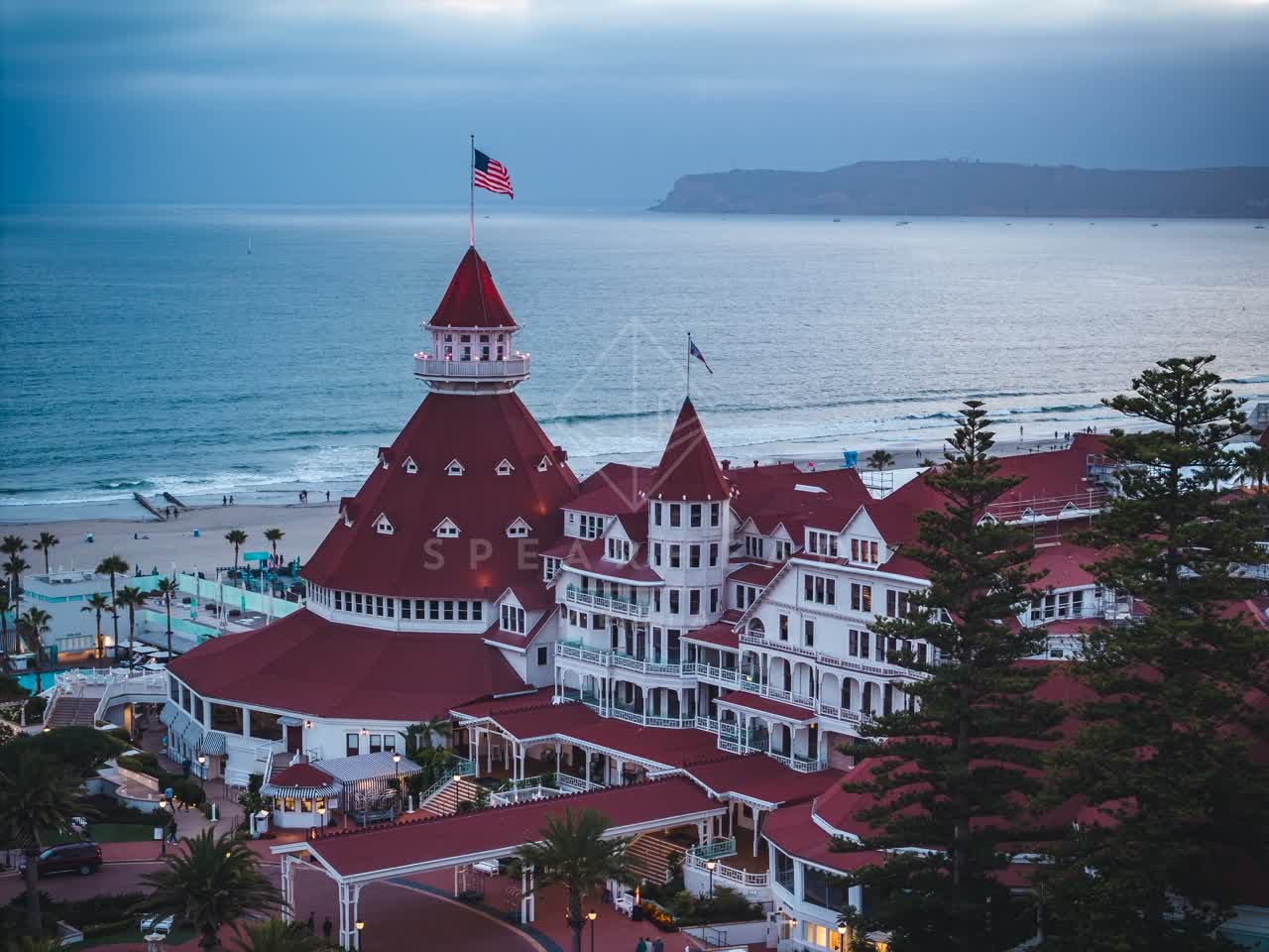 Low aerial view of the beach, palm trees and the ocean at Coronado Beach, with people walking.
