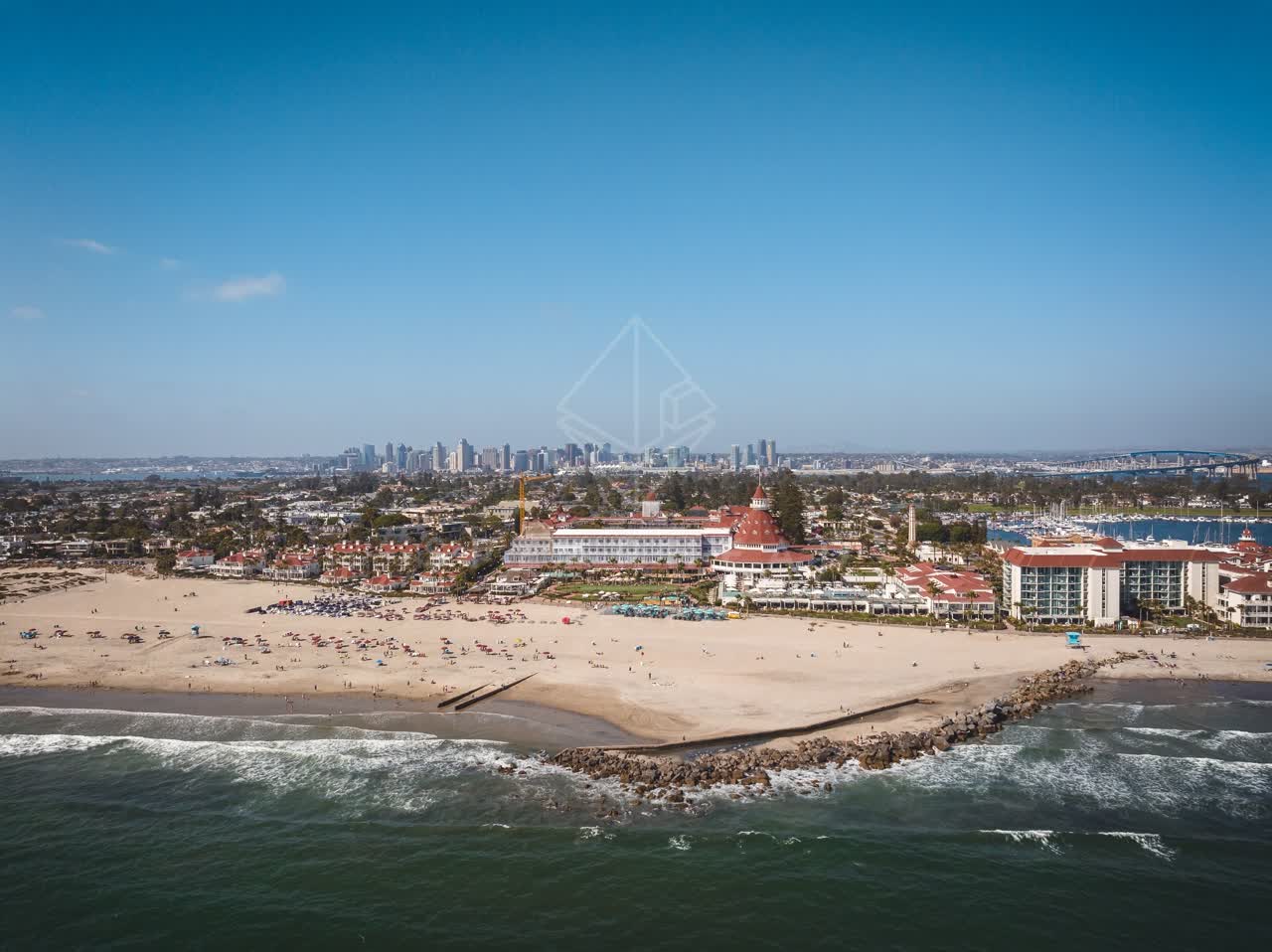 Aerial view of the beach, the skyline and boats at Coronado Beach, with people walking.