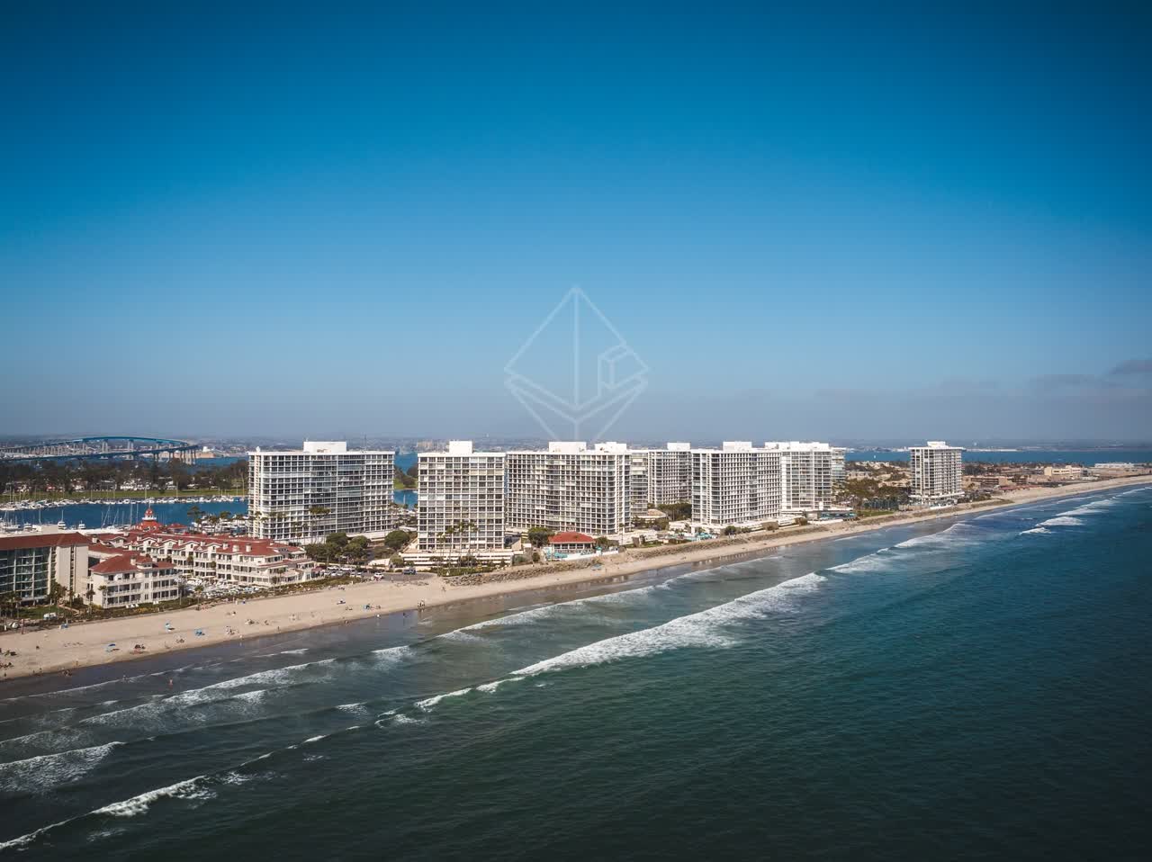 Aerial view of the beach, the surf and the bridge at Coronado Beach, with people walking.
