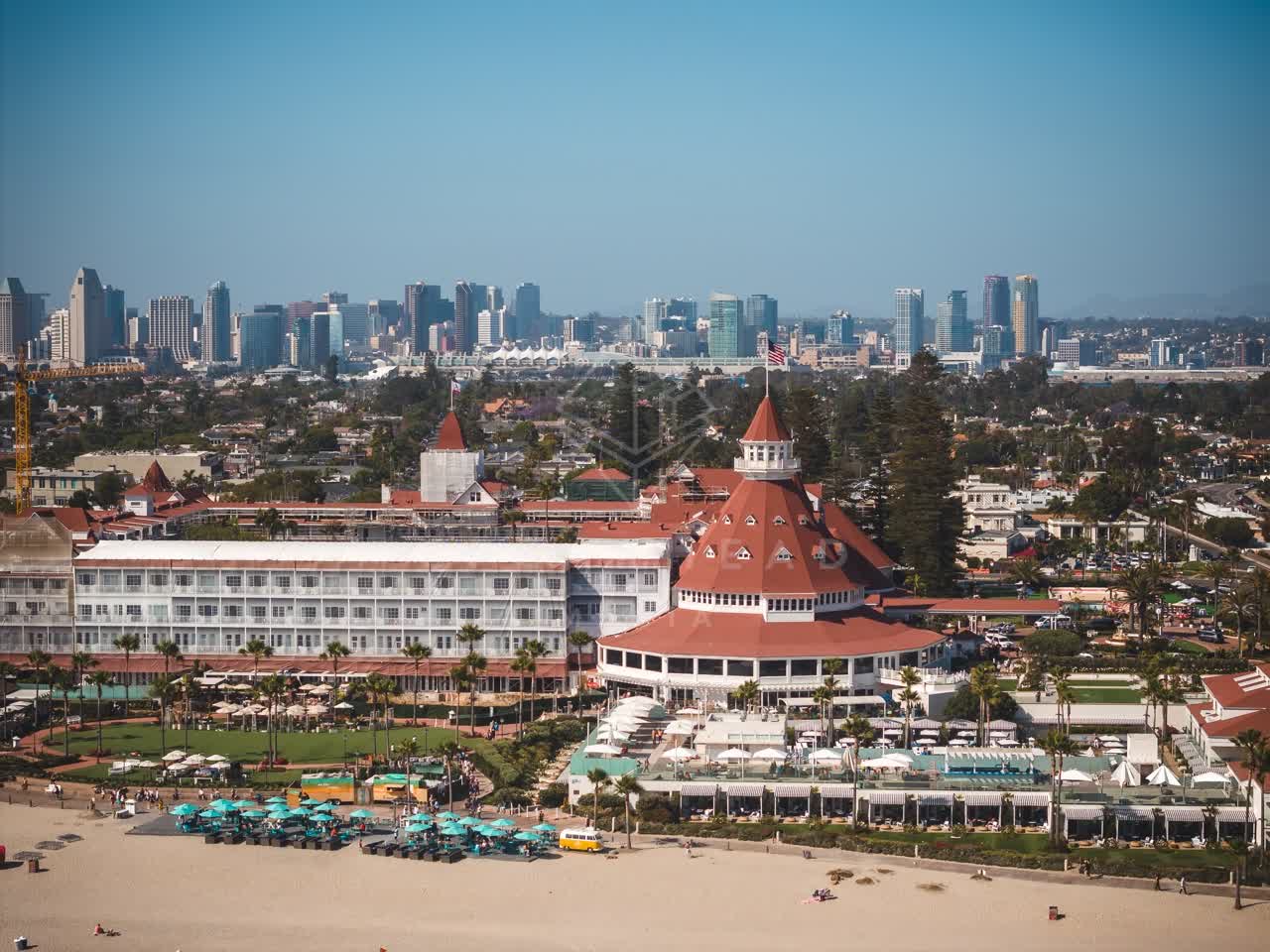 Aerial view of the beach, the skyline and palm trees at Coronado Beach, with a crowd gathered.