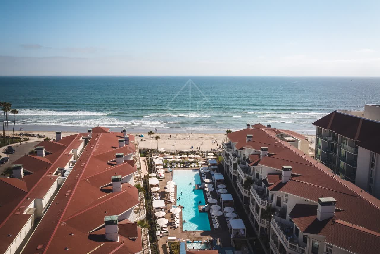 Aerial view of the beach, palm trees and the ocean at Coronado Beach, with swimmers in the water.