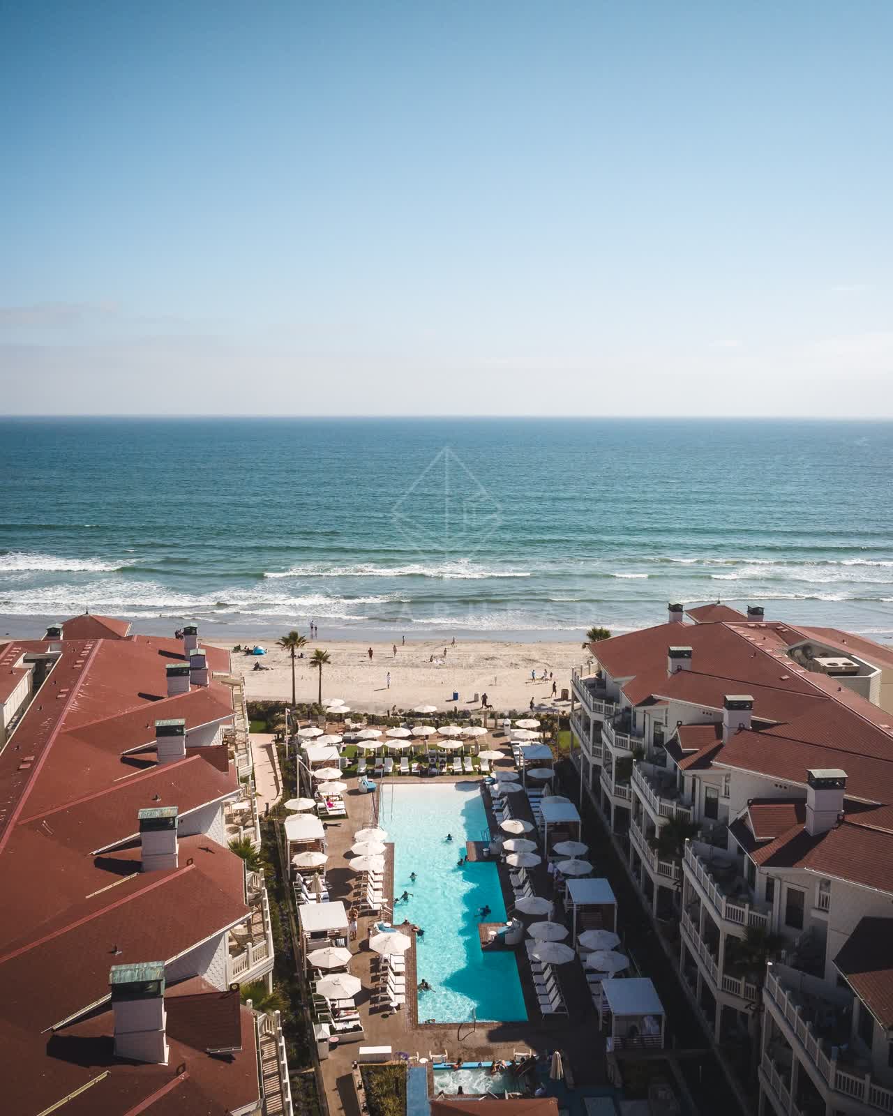 Aerial view of the beach, the pier and palm trees at Coronado Beach, with swimmers in the water.