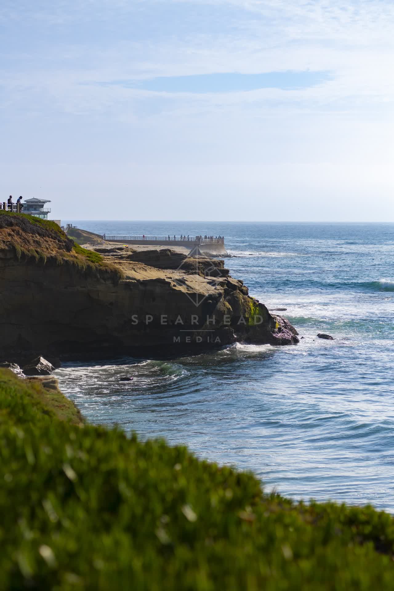 Elevated view of the cliffs, the surf and the ocean at La Jolla Cove, with people walking.