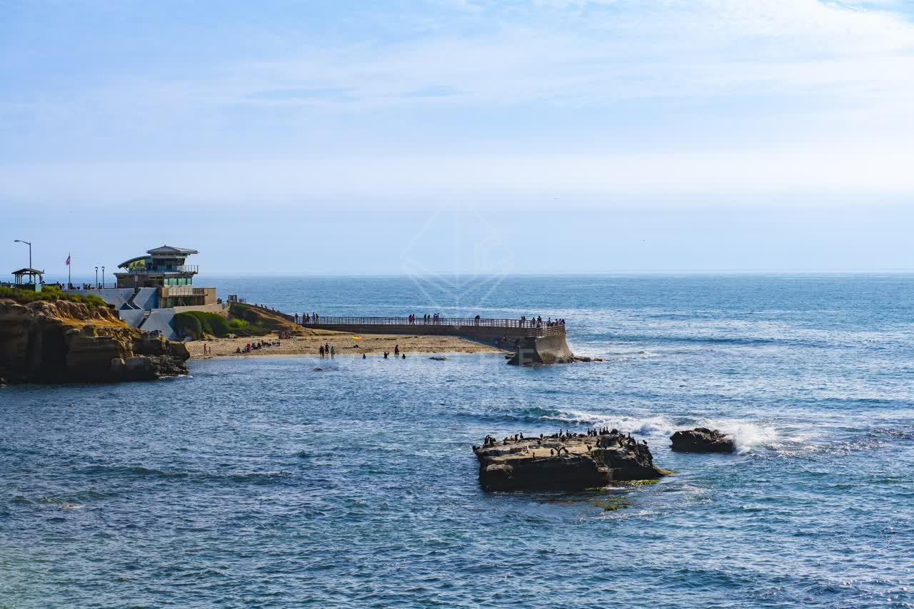 Elevated view of the cliffs, the pier and boats at La Jolla Cove, with people walking.