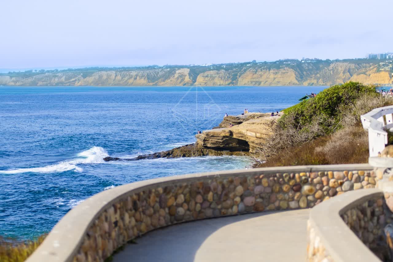 Elevated view of the cliffs, the surf and the ocean at La Jolla Cove, with people walking.